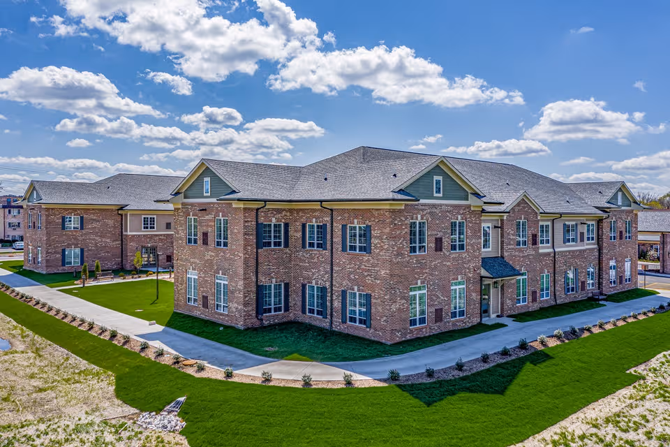 Brick senior living facility with a curved driveway and manicured green lawns.