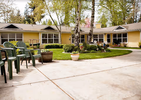 Yellow single-story senior living facility with a paved courtyard and outdoor chairs.
