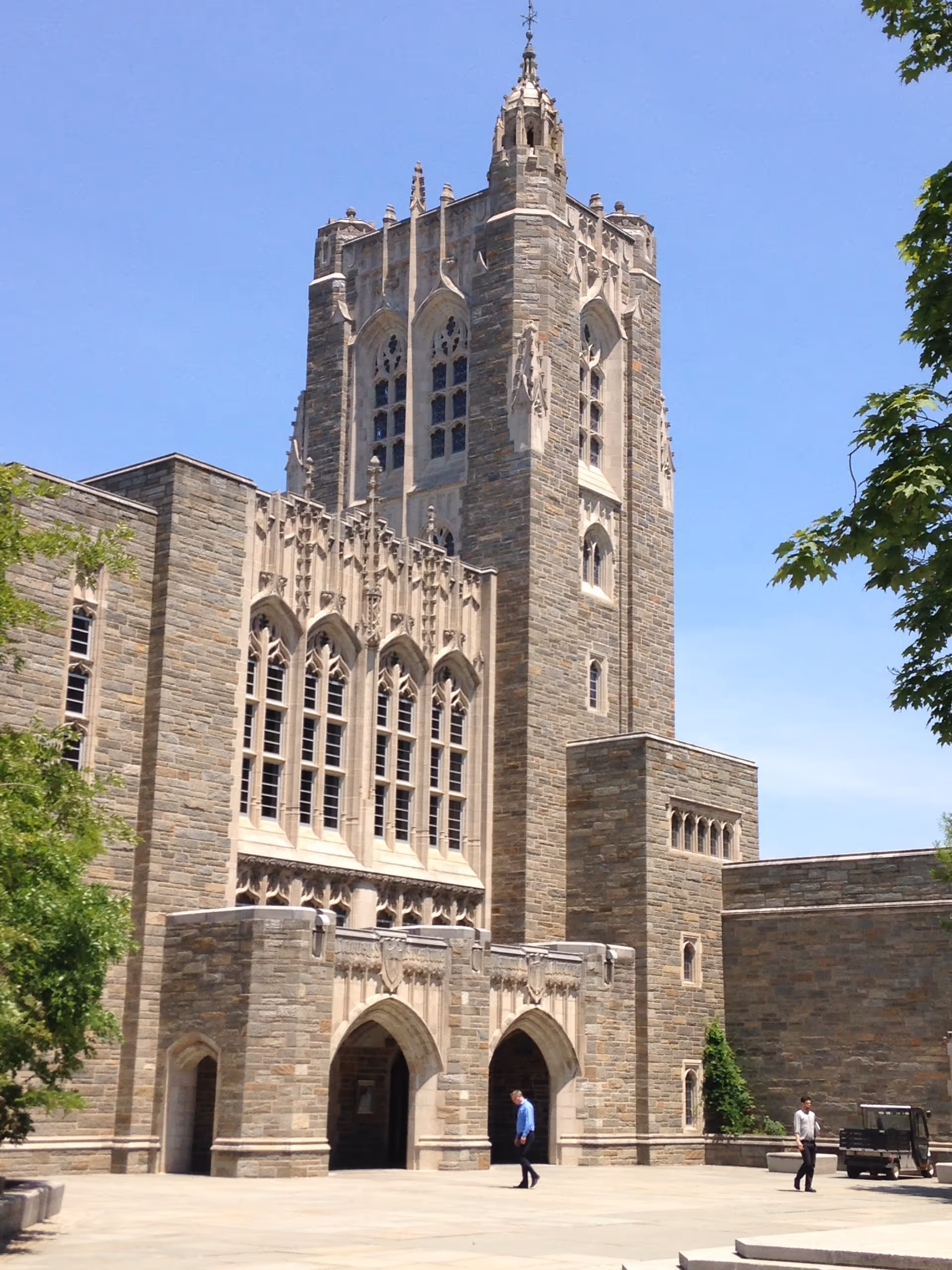 Gothic stone building with a tall tower and arched entrance against a blue sky.