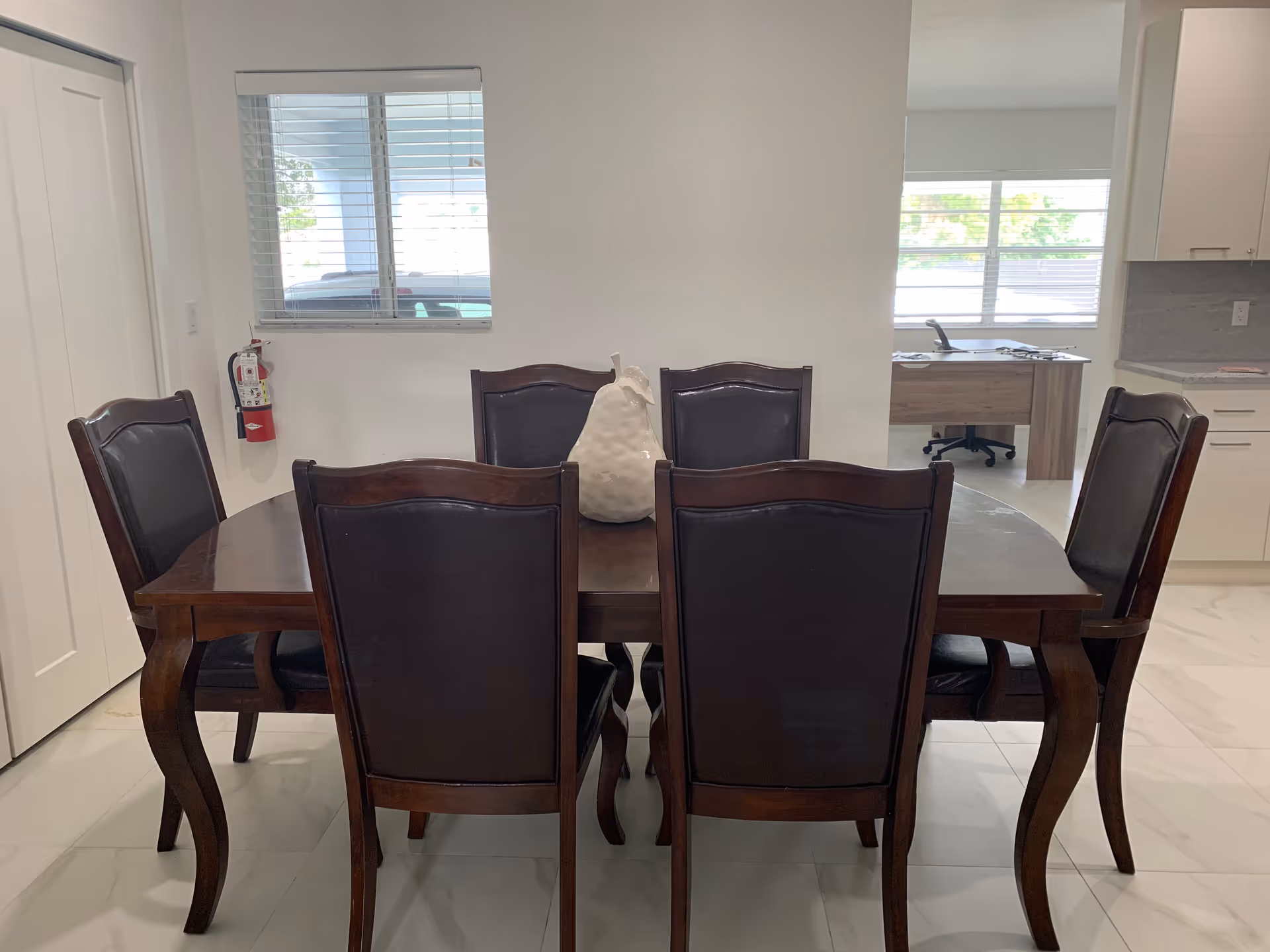 A wooden dining table with six upholstered chairs and a centerpiece in a bright dining area.