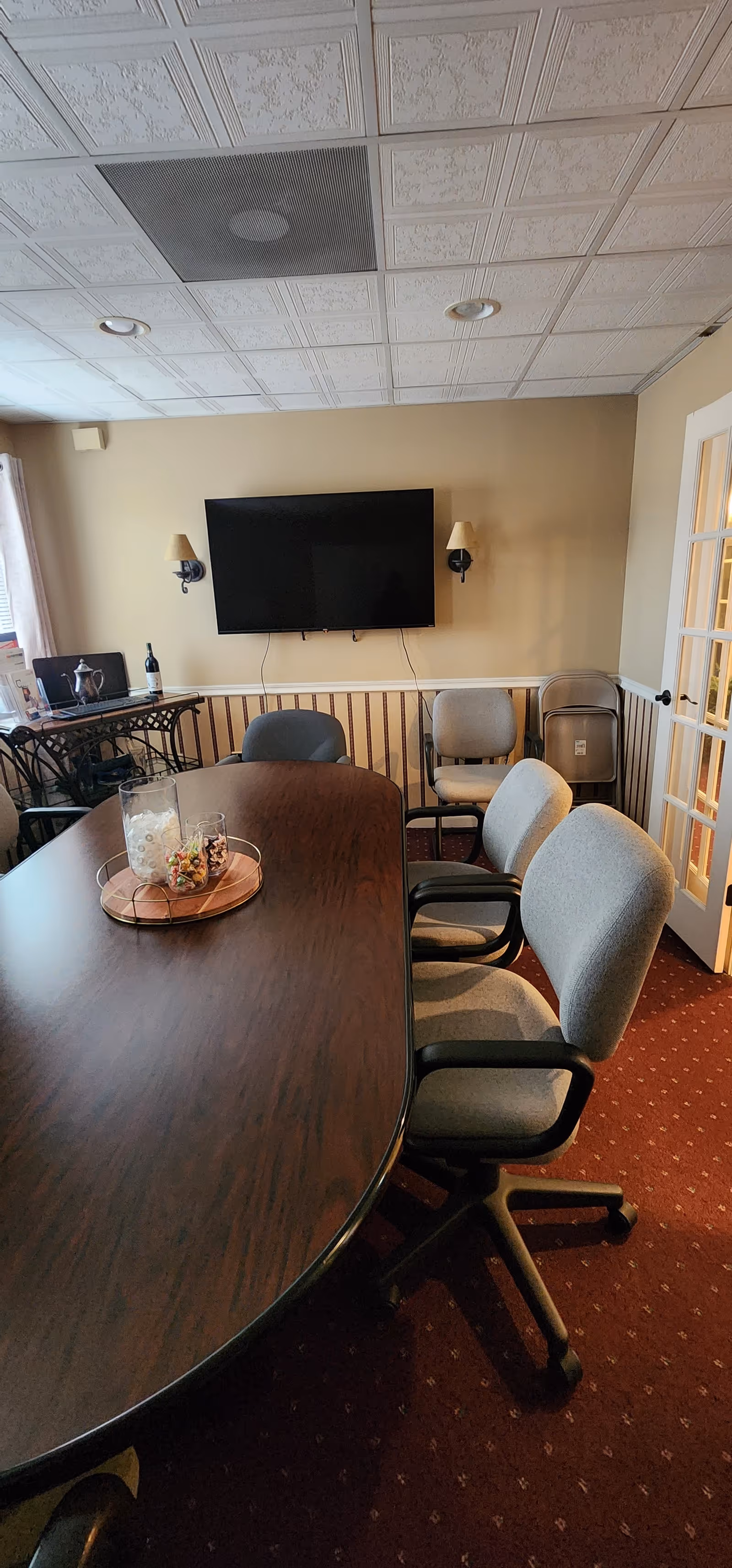 There is a long dark wood table with chairs in a furnished senior living common room.