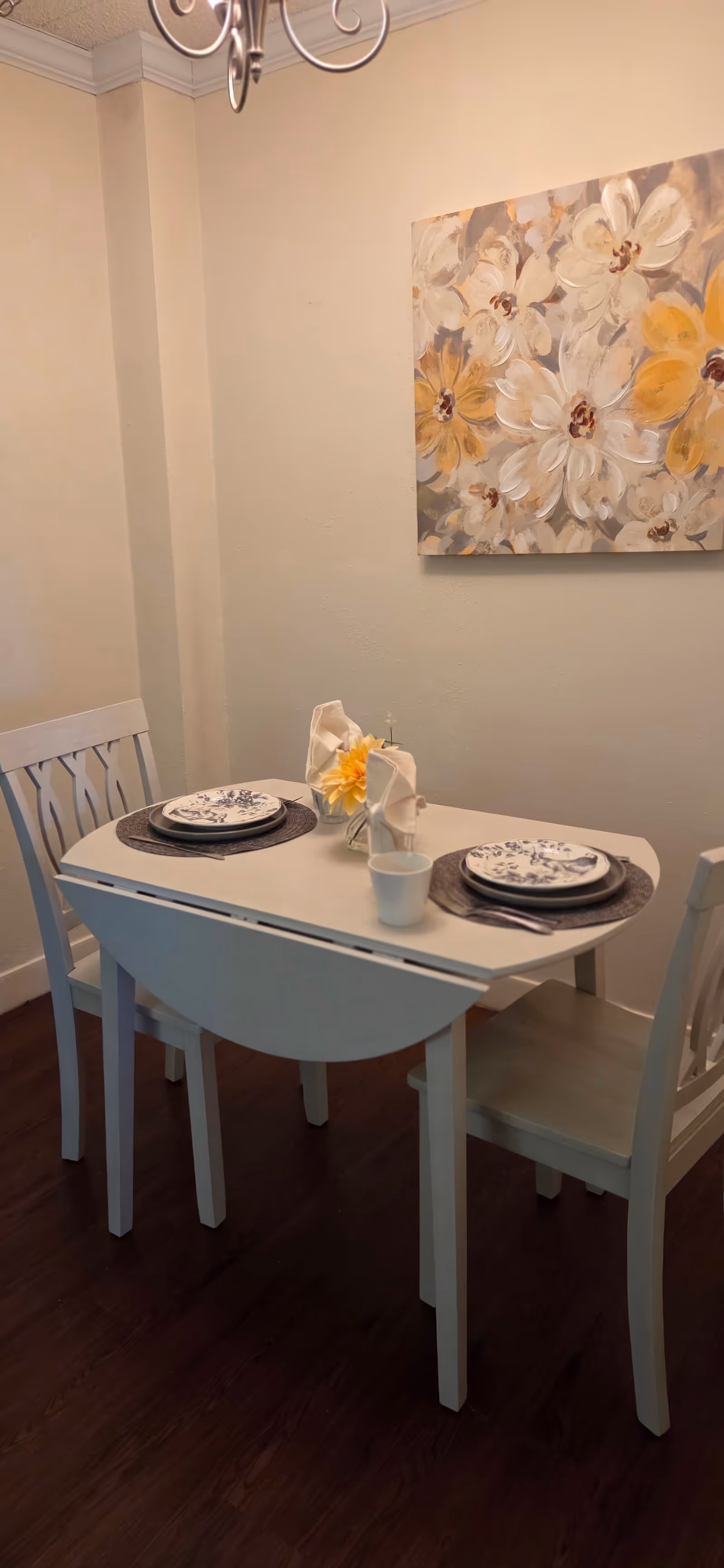 A small dining nook with a two-person table, plates, and floral wall art.