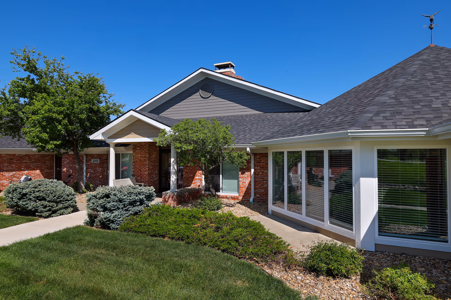 Brick assisted living facility exterior with a covered entrance, windows, and landscaped shrubs.