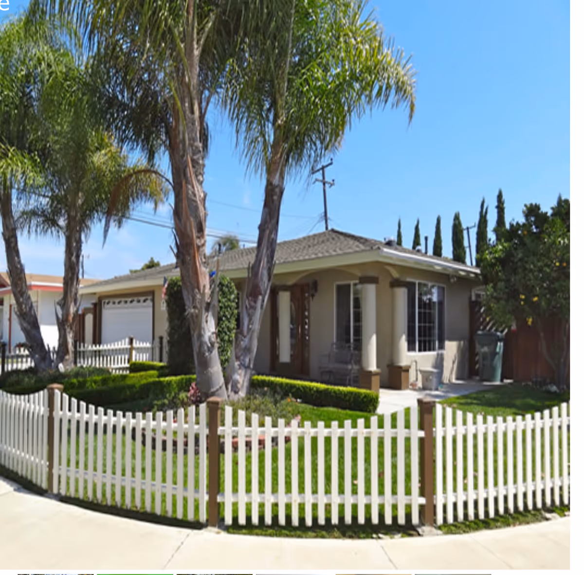 Front view of a single-story home with a white picket fence and palm trees.
