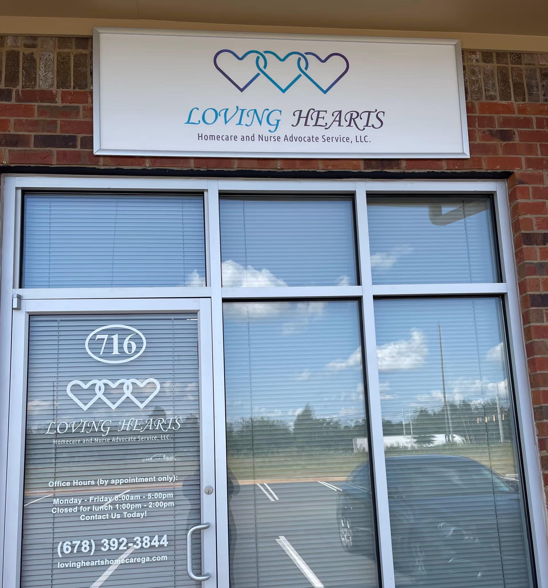 Exterior view of Loving Hearts facility with sign, brick facade, glass doors, and parked cars.