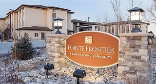 Stone entrance sign reading "Pointe Frontier A Senior Living Community" with lamps, rock landscaping, and the facility building in the background.