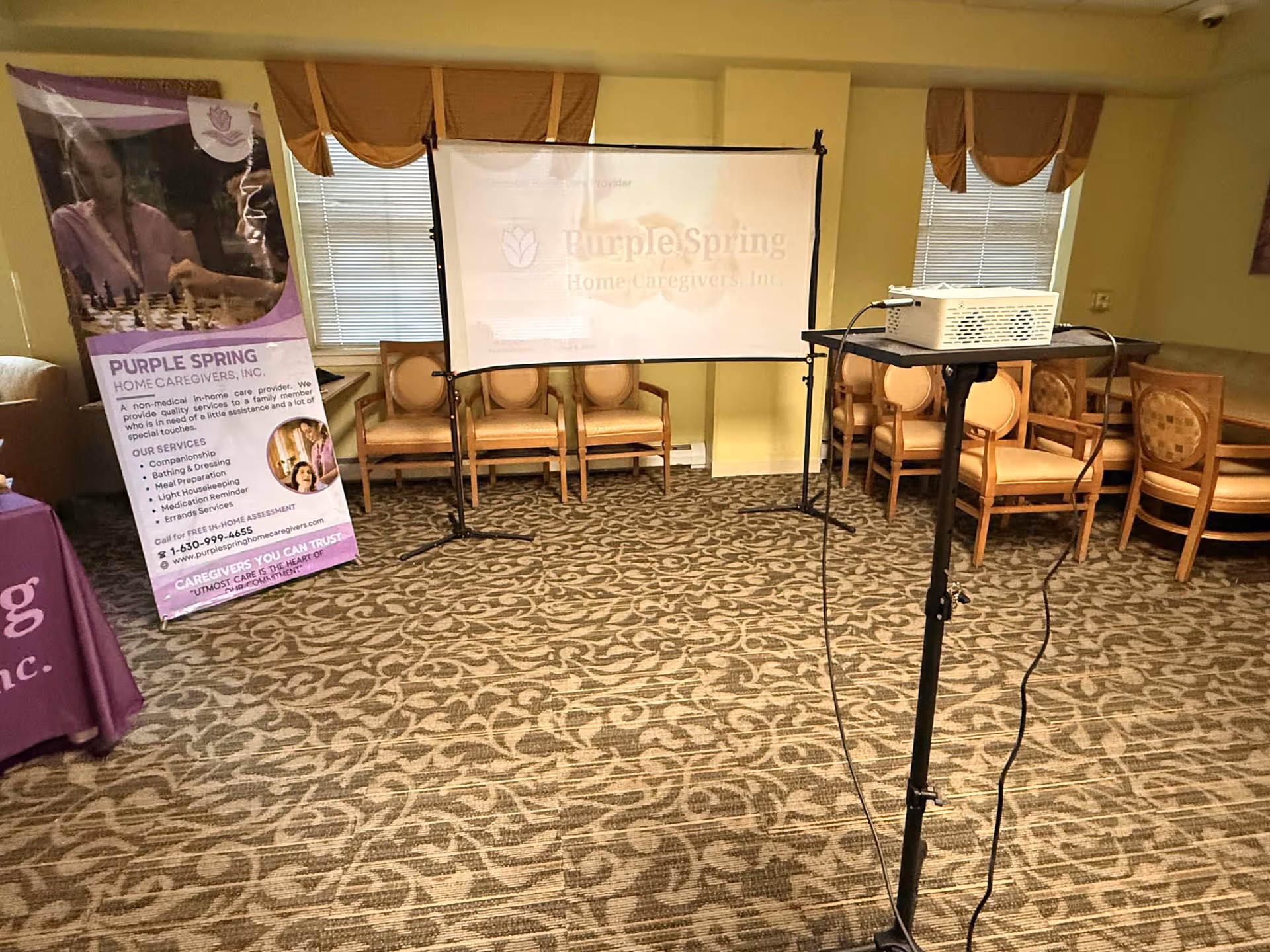 A projector, screen, and chairs set up for a Purple Spring Home Caregivers presentation.