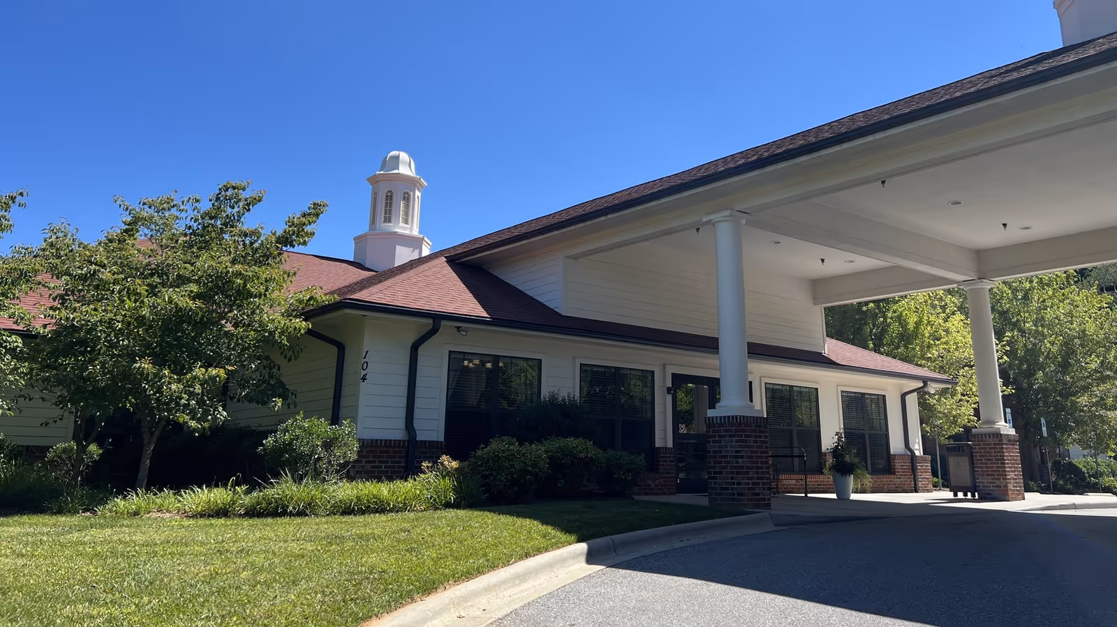 Front exterior of Pisgah Manor with a covered entrance, white siding, brick columns, and landscaping.