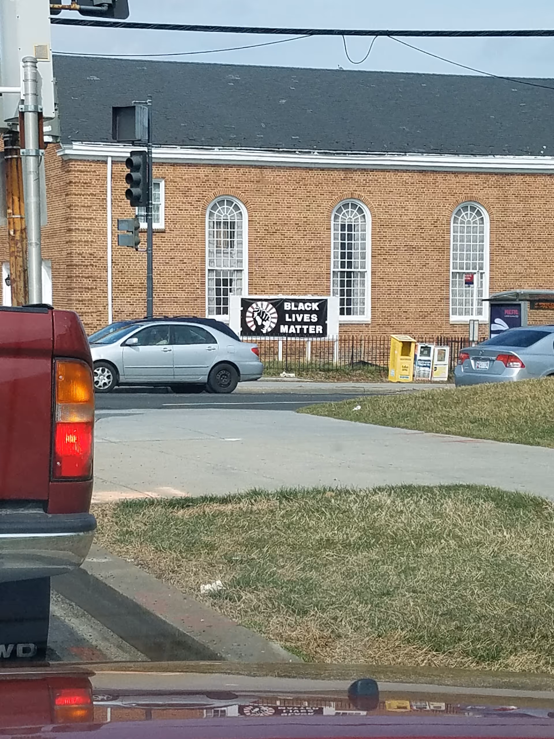 Brick building with arched windows along a street, cars parked, and a Black Lives Matter sign.