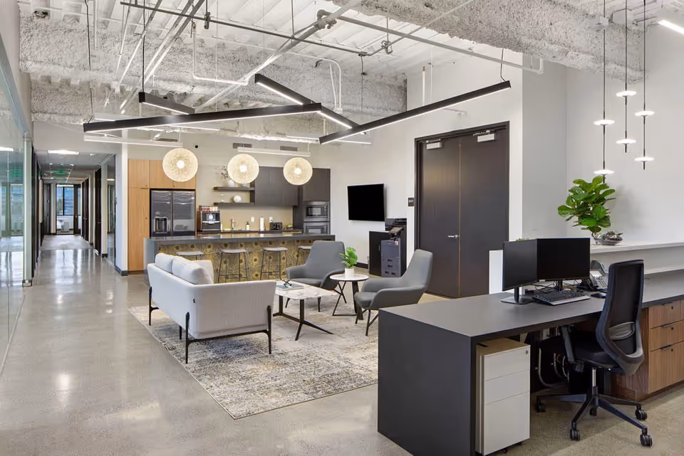 Modern open lounge area with kitchenette bar, seating, and a reception desk.