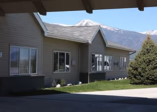 Exterior view of a senior living facility with beige siding, windows, and distant mountains.