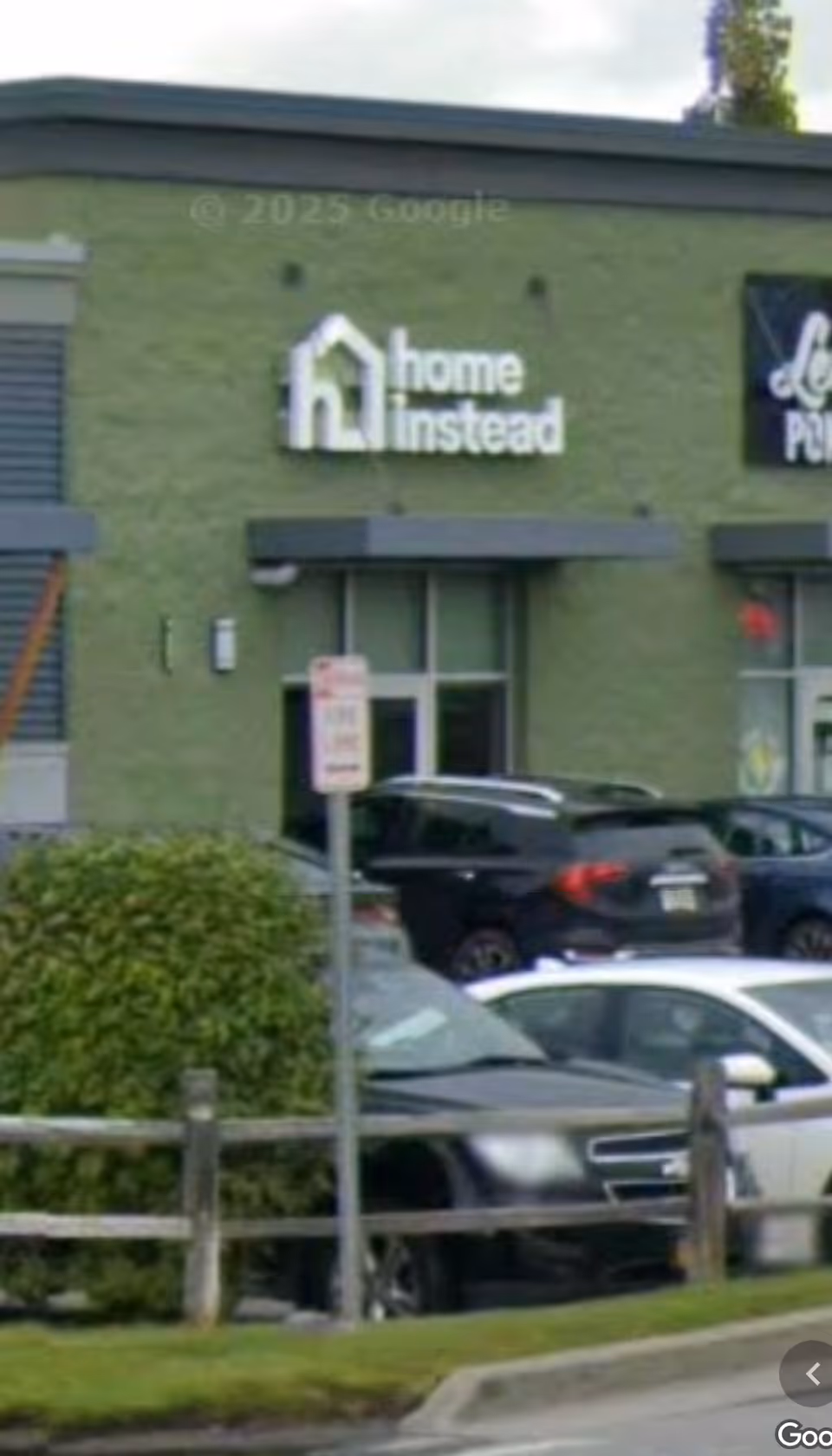 Exterior of a green building with a Home Instead sign and parked cars.