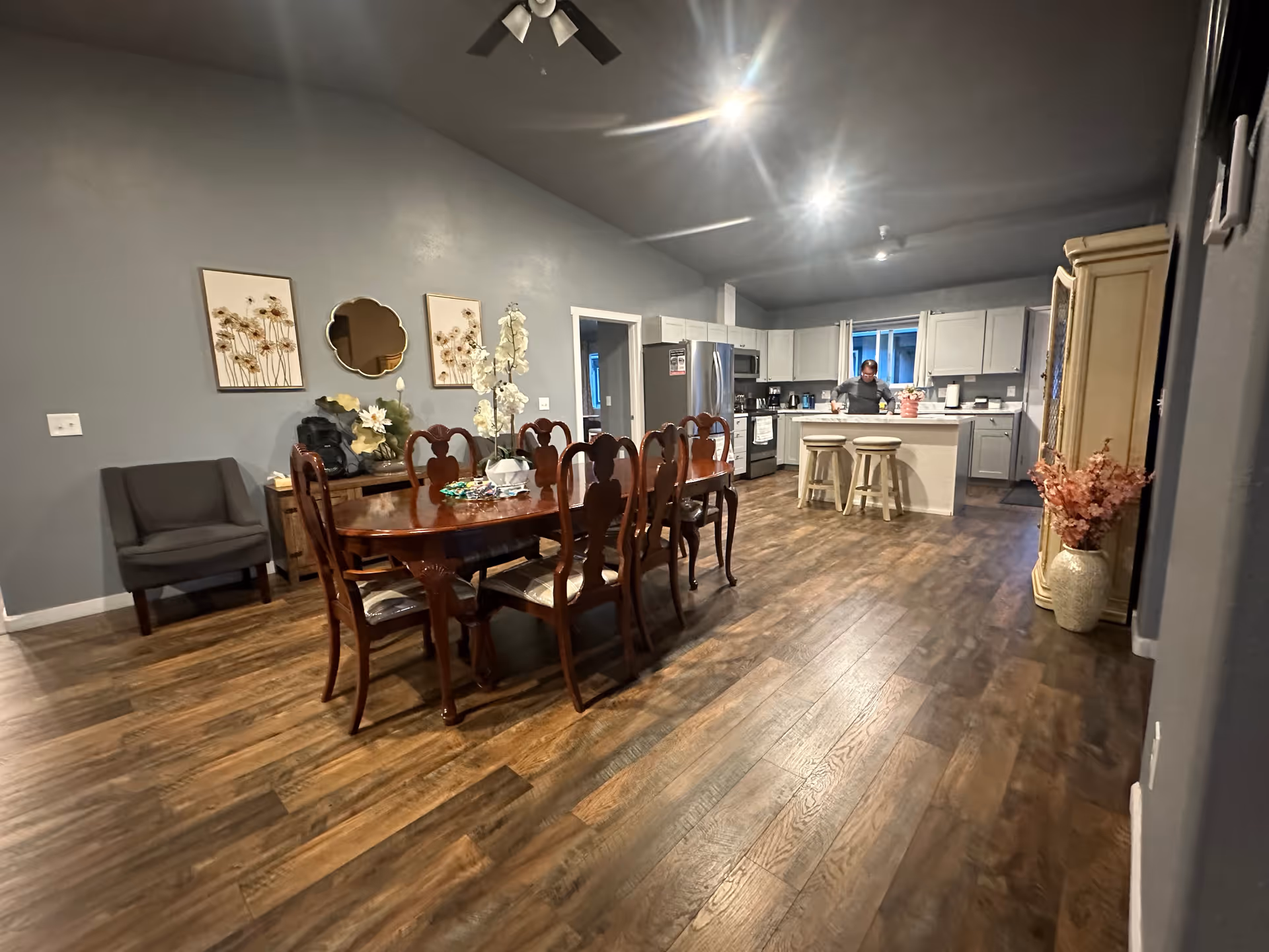 Spacious dining area and kitchen with wooden table, chairs, and stools in a homey facility.