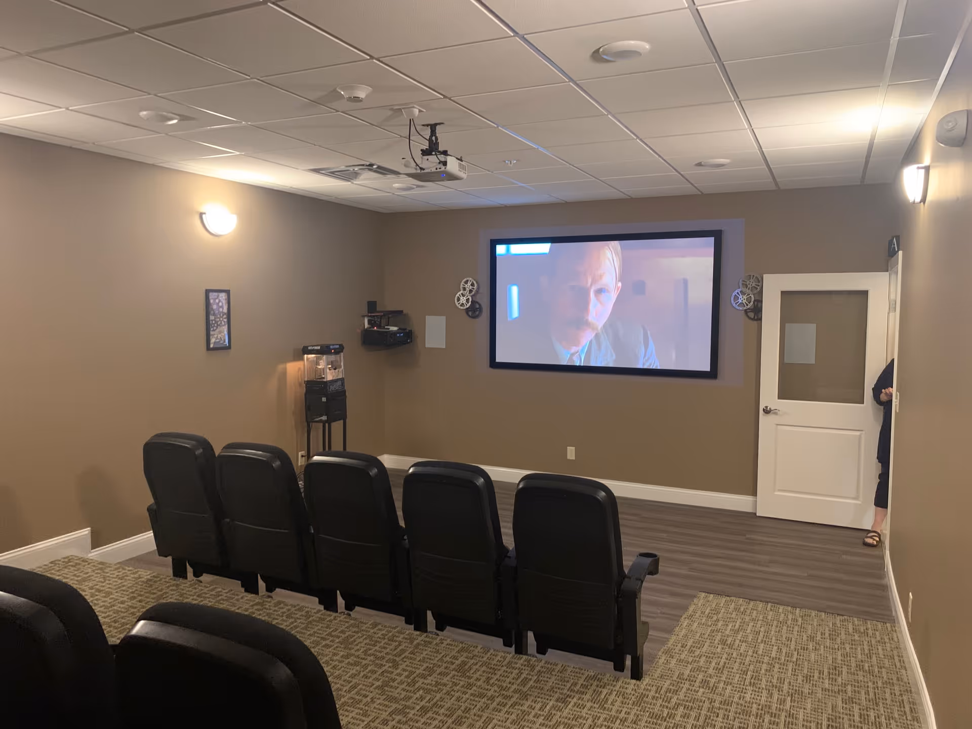 A small theater-style room with rows of black chairs facing a wall-mounted screen.
