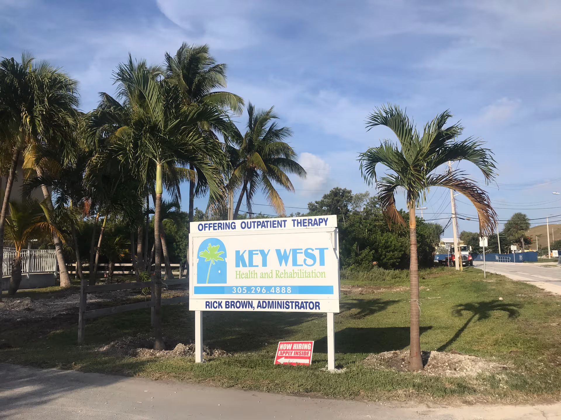 Outdoor scene with palm trees and a sign advertising health and rehabilitation services.