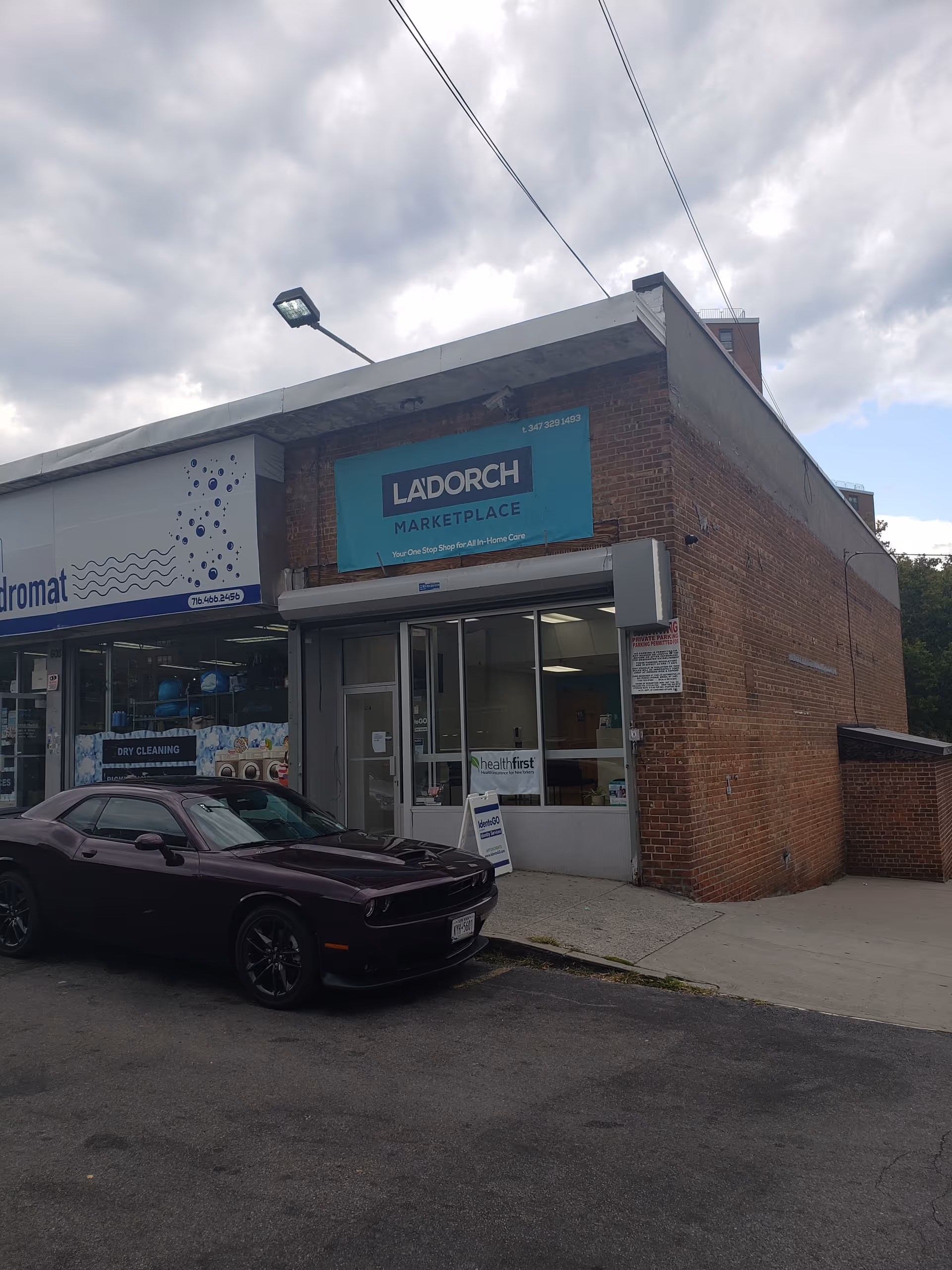 Brick storefront with a La'Dorch Marketplace sign and a black car parked outside.