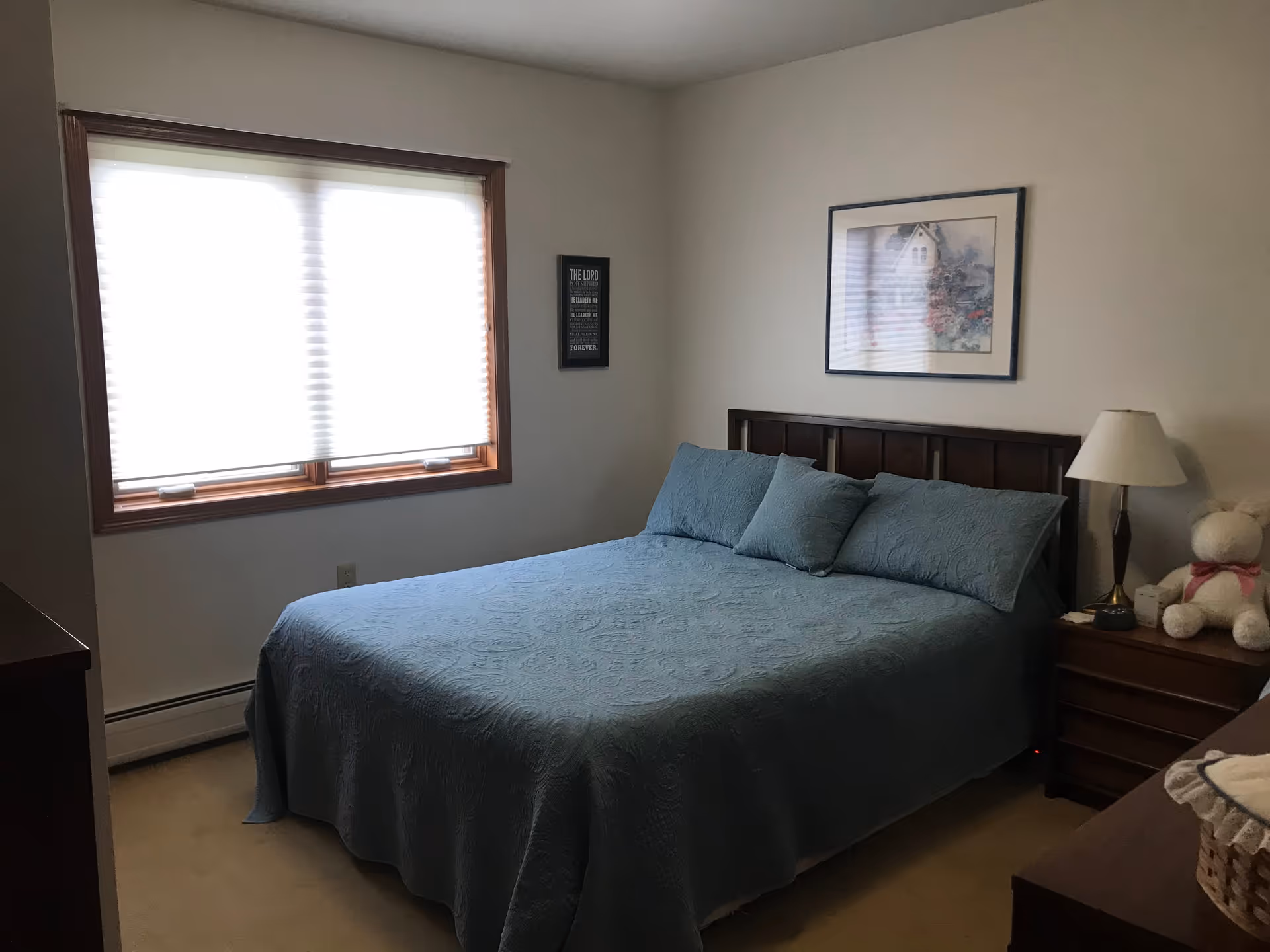 A neatly made blue bed with two nightstands and a teddy bear in a cozy bedroom.