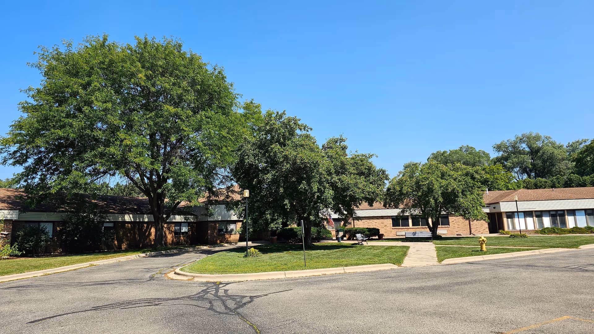 Exterior view of a single-story brick senior living facility with trees and a road in front.