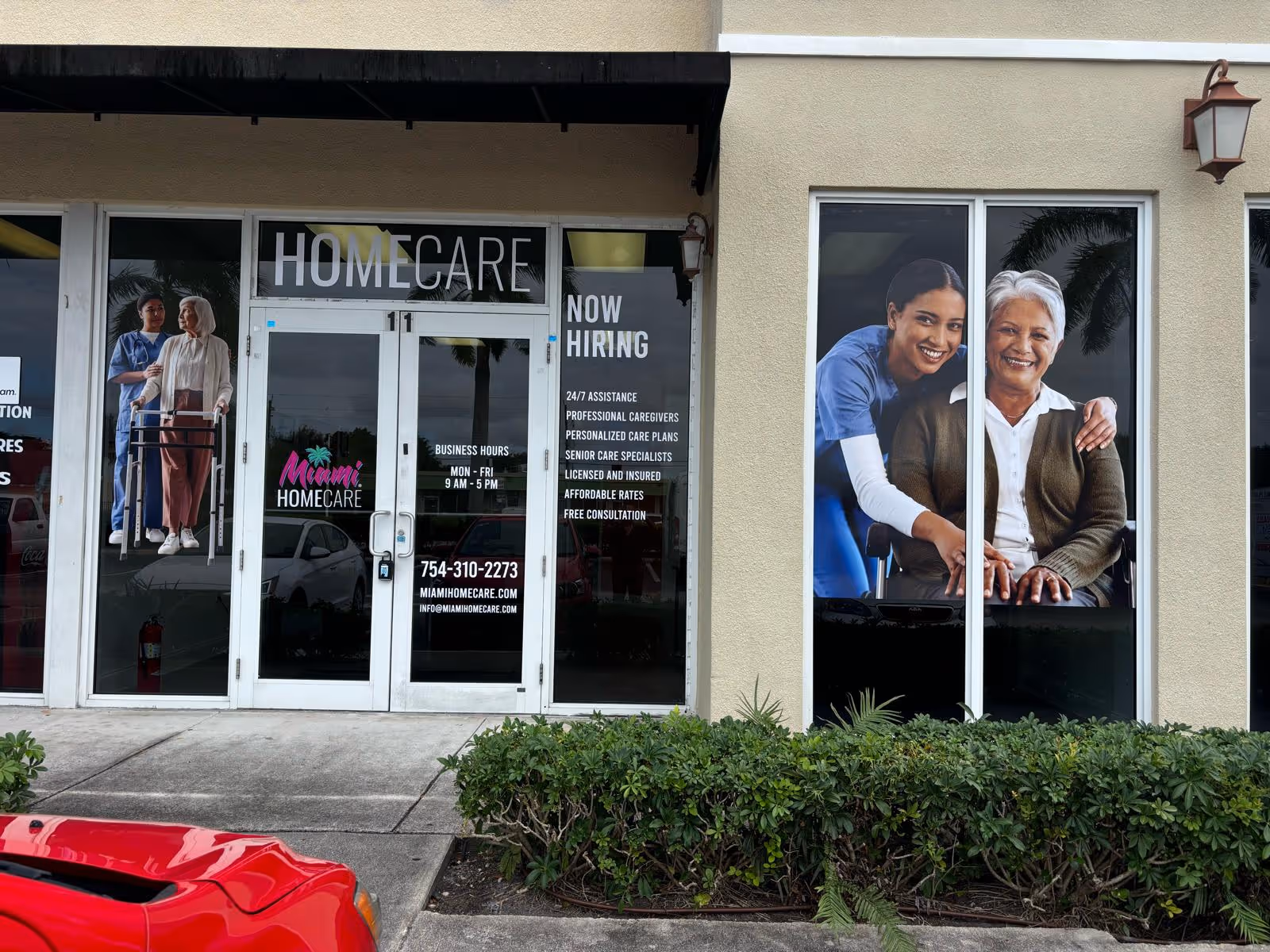Storefront of Miami Home Care with glass doors, Now Hiring sign, and caregiver posters.