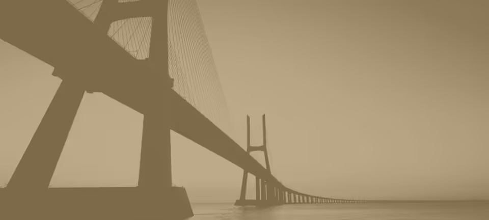 A long bridge spans over calm water beneath a hazy sky.