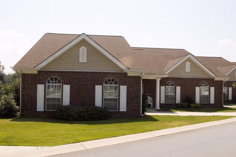 Single-story brick senior living building with white shutters and manicured lawn.