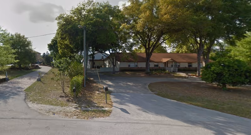 Single-story assisted living building with a circular driveway and large trees in front.