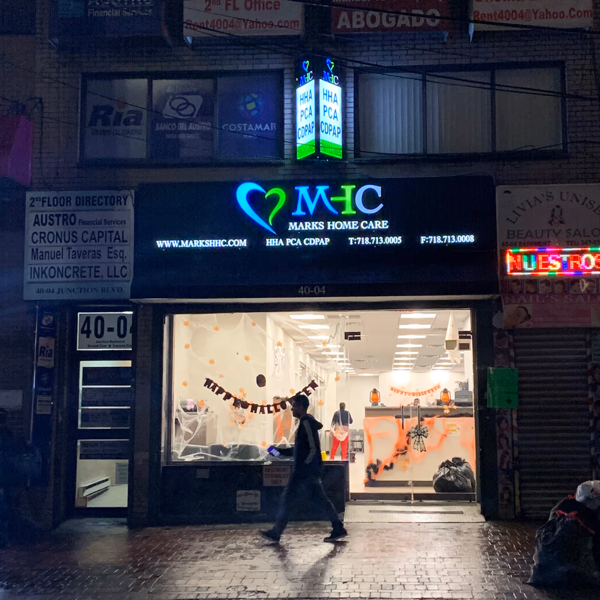 Nighttime storefront with illuminated Marks Home Care sign and a pedestrian outside.