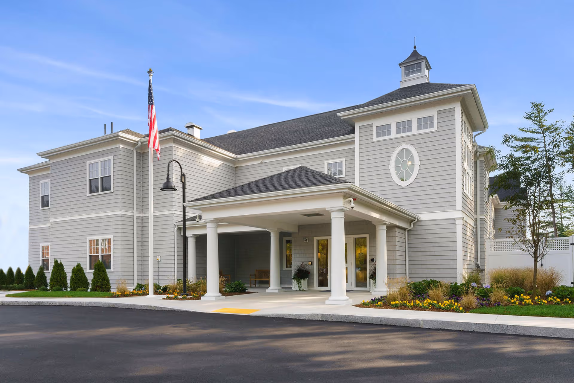 Exterior view of The Village at Duxbury, a gray senior living facility with a covered entrance.