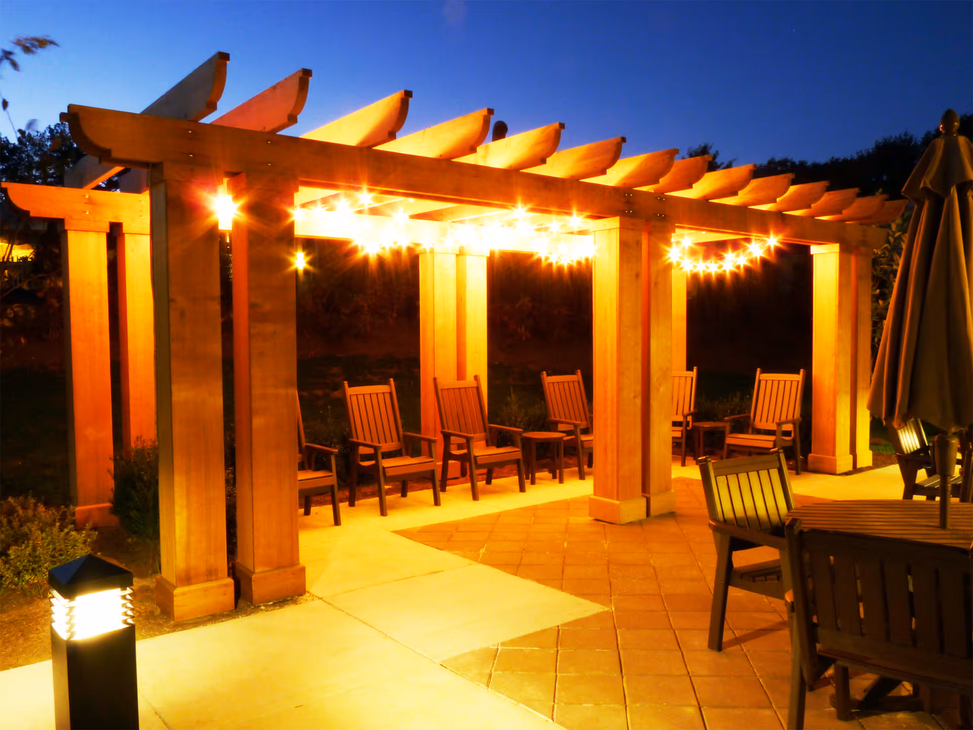 Outdoor patio under a wooden pergola with string lights and seating.