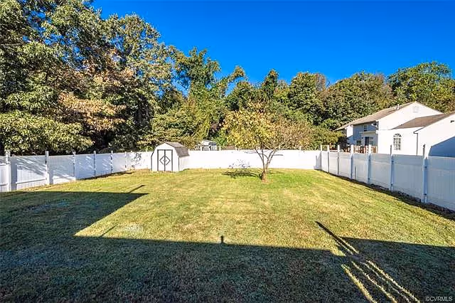 Fenced backyard with a small shed, a single tree, and a mowed lawn under a clear blue sky.