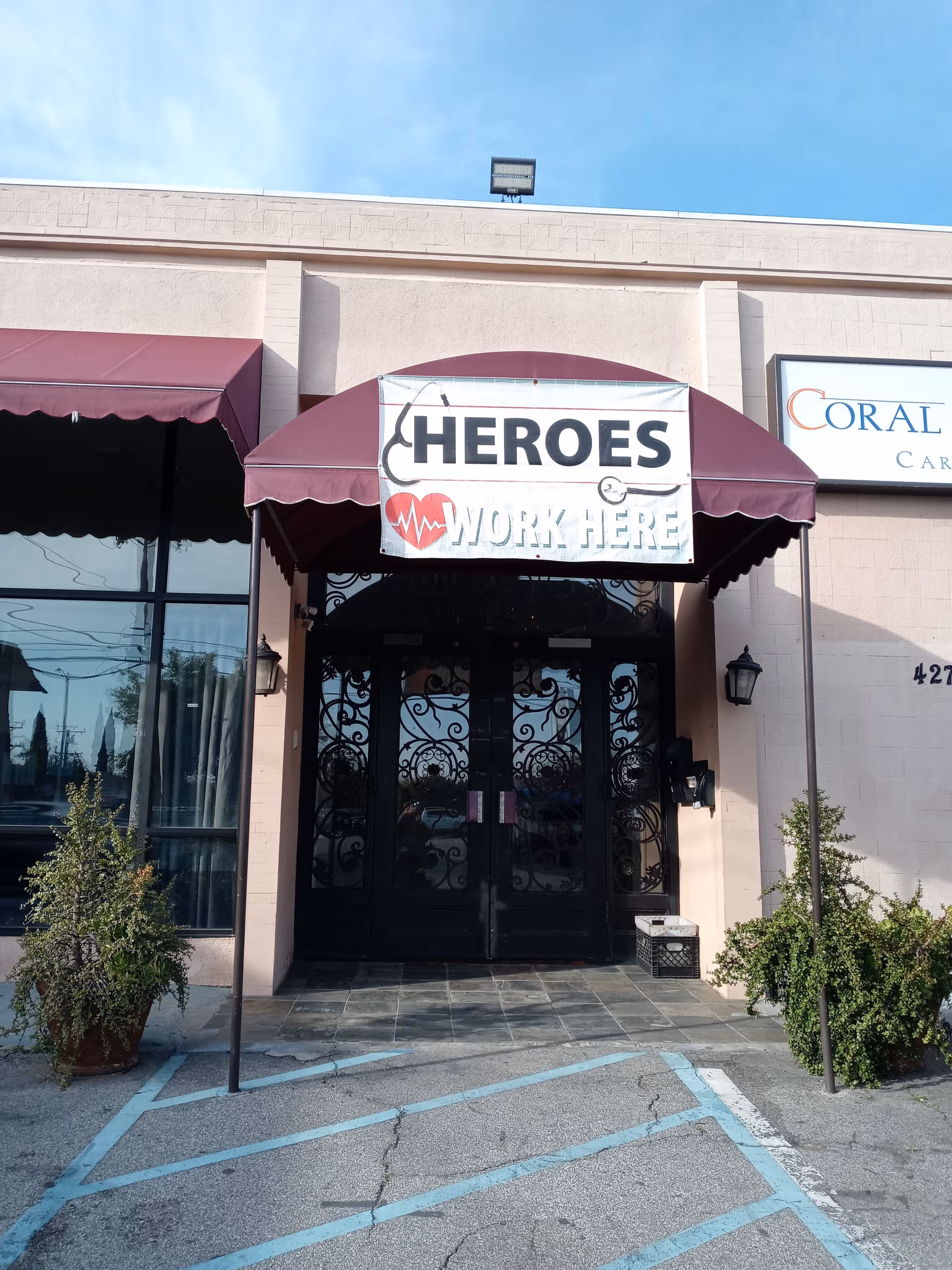 Entrance of Coral Oaks Care Living featuring maroon canopy and Heroes Work Here banner