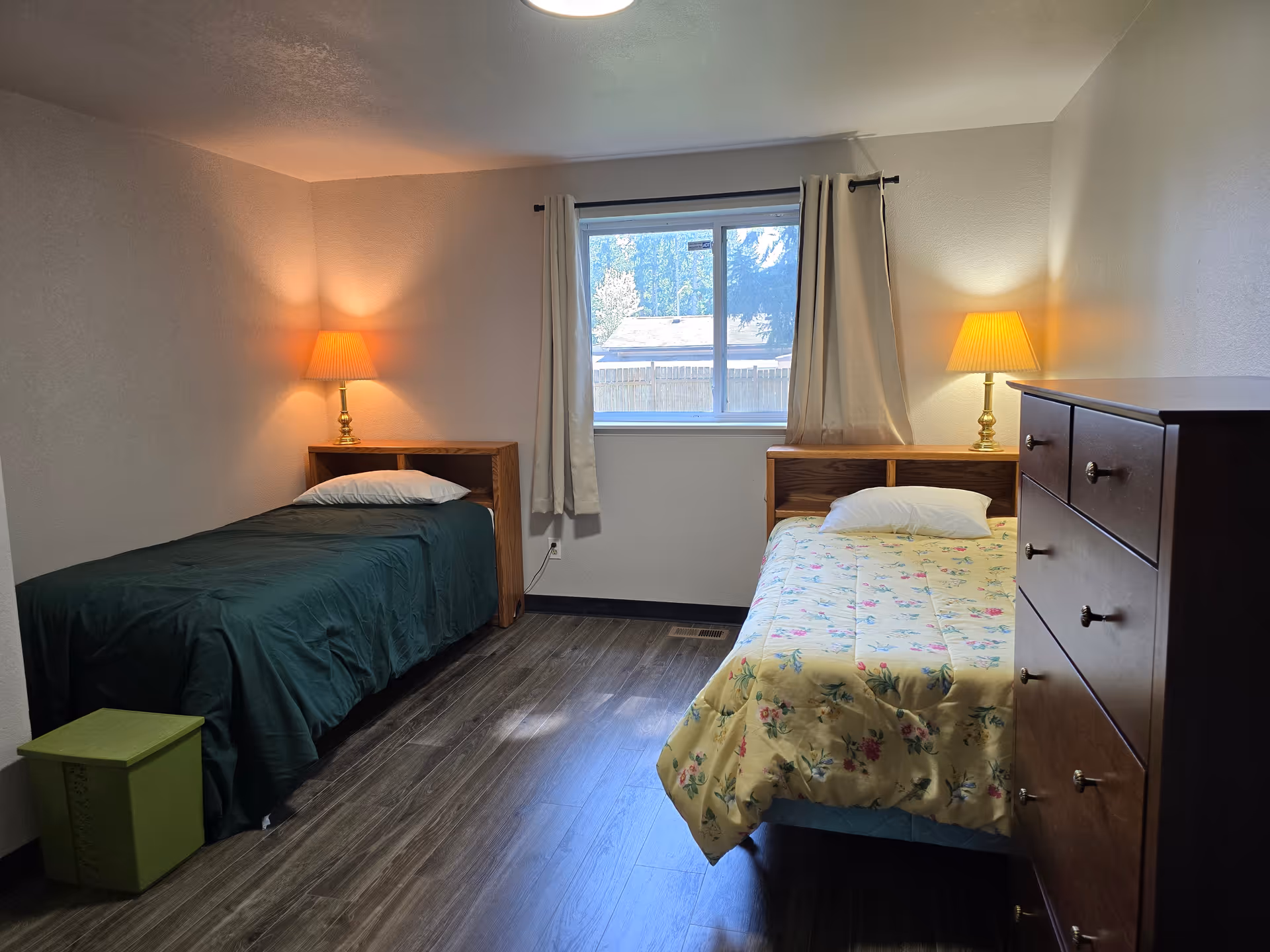 Two single beds with nightstands, lamps, and a dresser in a cozy bedroom.