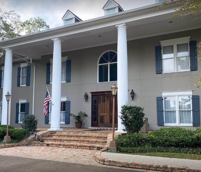 Colonial-style building front with tall white columns, brick steps, and an American flag