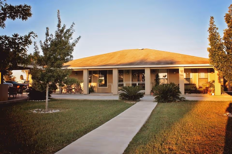 Single-story building with a front walkway leading to a covered porch, lawn, and trees.