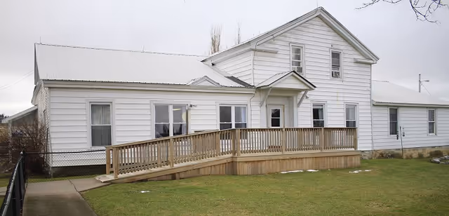White, single-story building with a wooden ramp and grassy front yard.