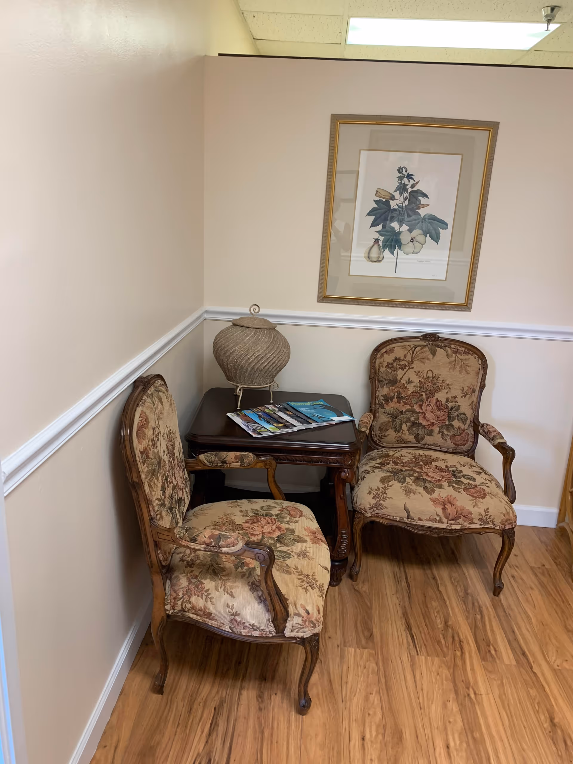 Two floral upholstered chairs sit beside a small dark table with magazines and a decorative vase.