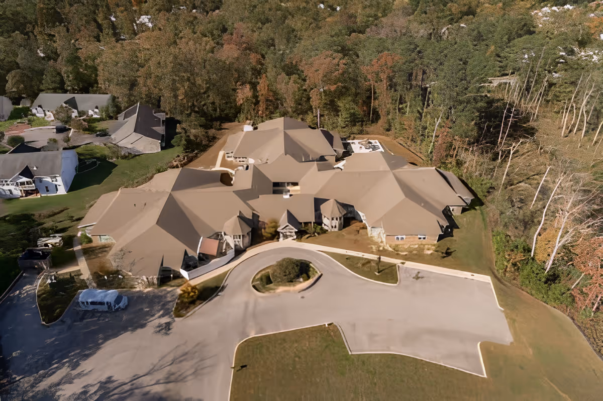 Aerial view of a large senior living facility building surrounded by trees and greenery, with a circular driveway and parking area in front.