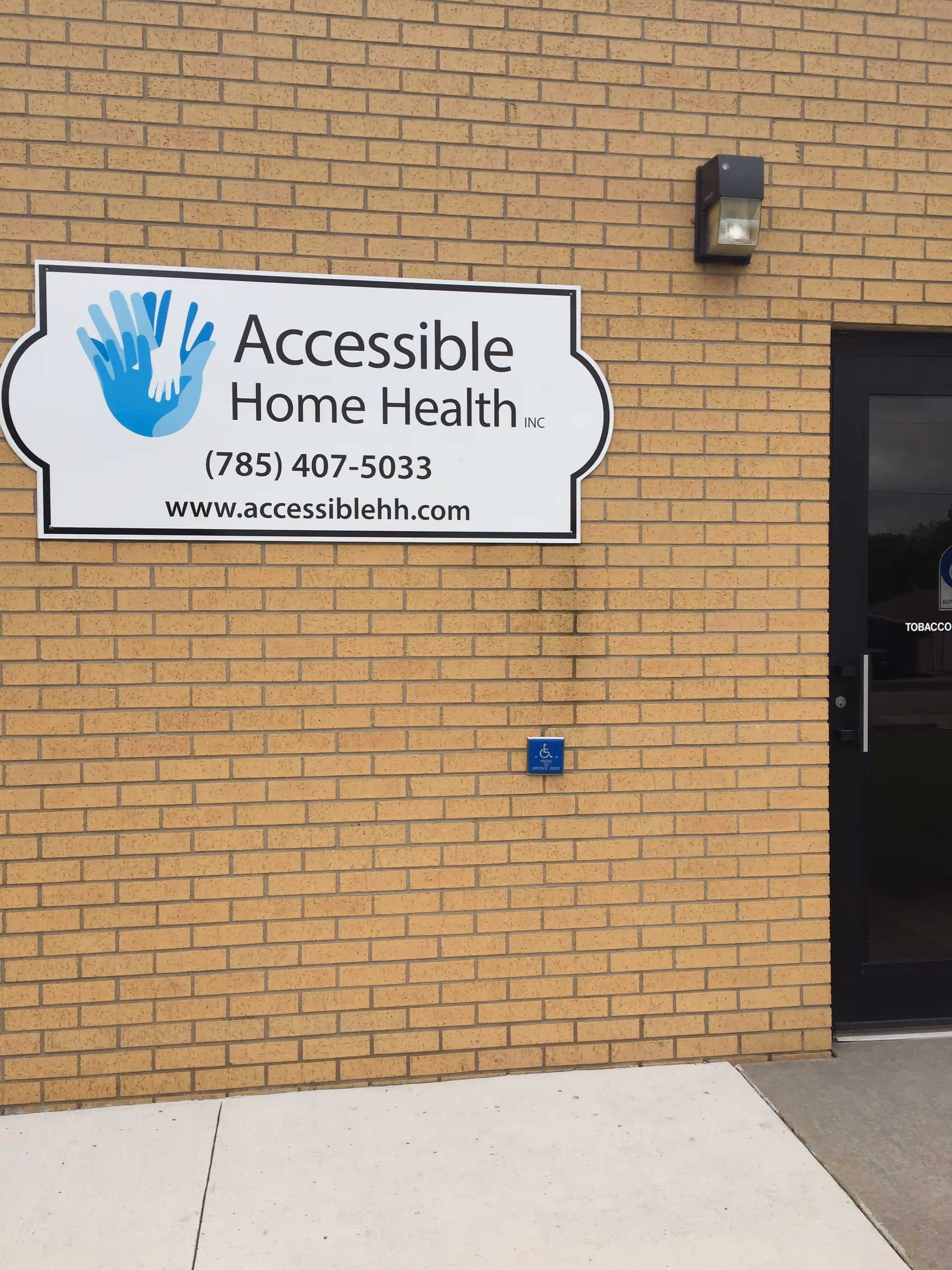 Brick exterior wall with Accessible Home Health sign and a nearby entrance door.