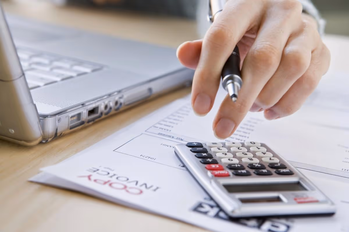 Close-up of a hand using a calculator beside a laptop on a desk.