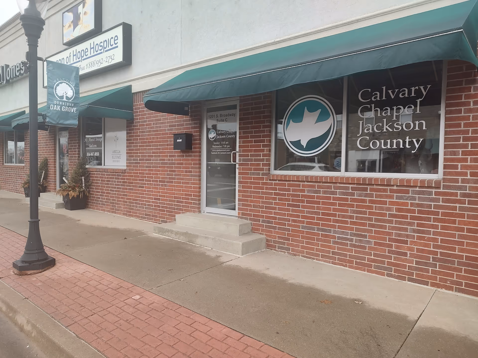 Brick storefront with green awnings and Beacon of Hope Hospice signage along the sidewalk.