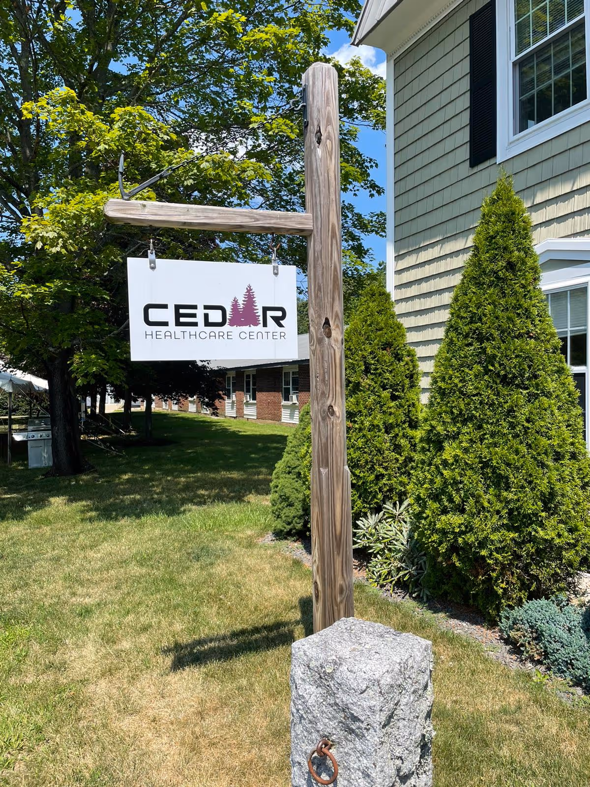 Exterior view of a Cedar Healthcare Center sign mounted on a wooden post.