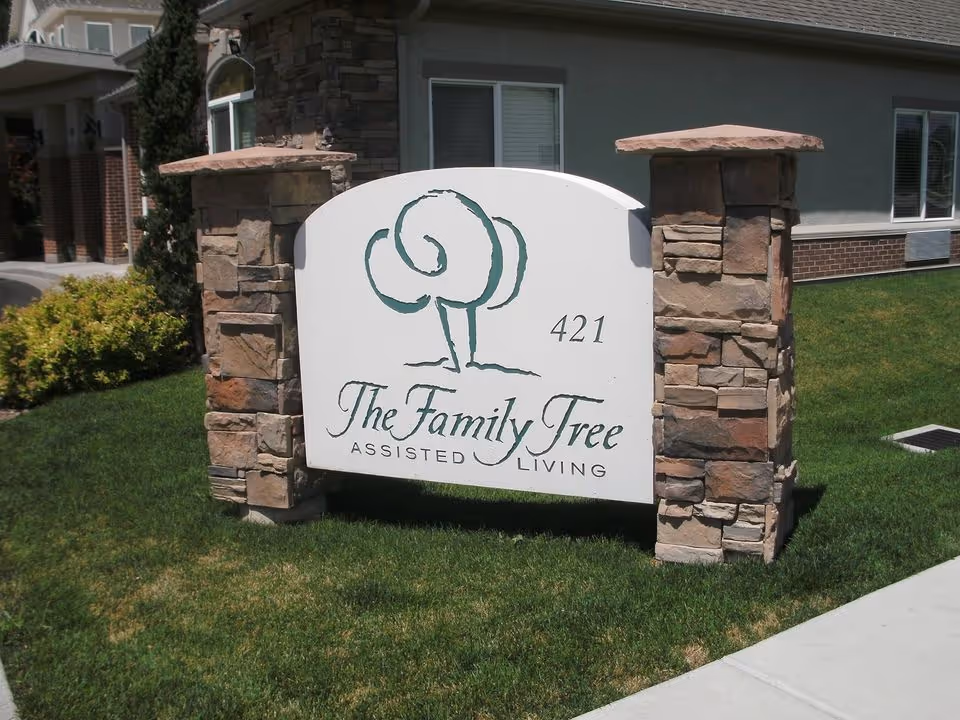 Outdoor sign for The Family Tree Assisted Living with the number 421, mounted between two stone pillars on a grassy area in front of a building.