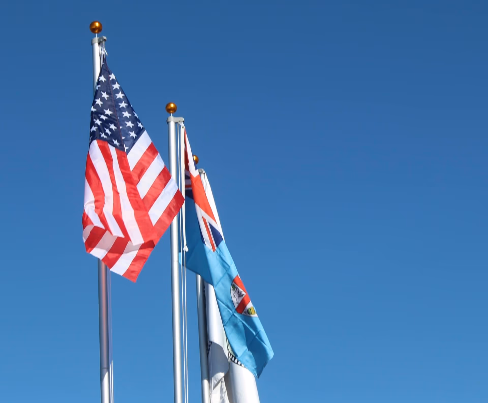 Three flagpoles with flags against a clear blue sky.