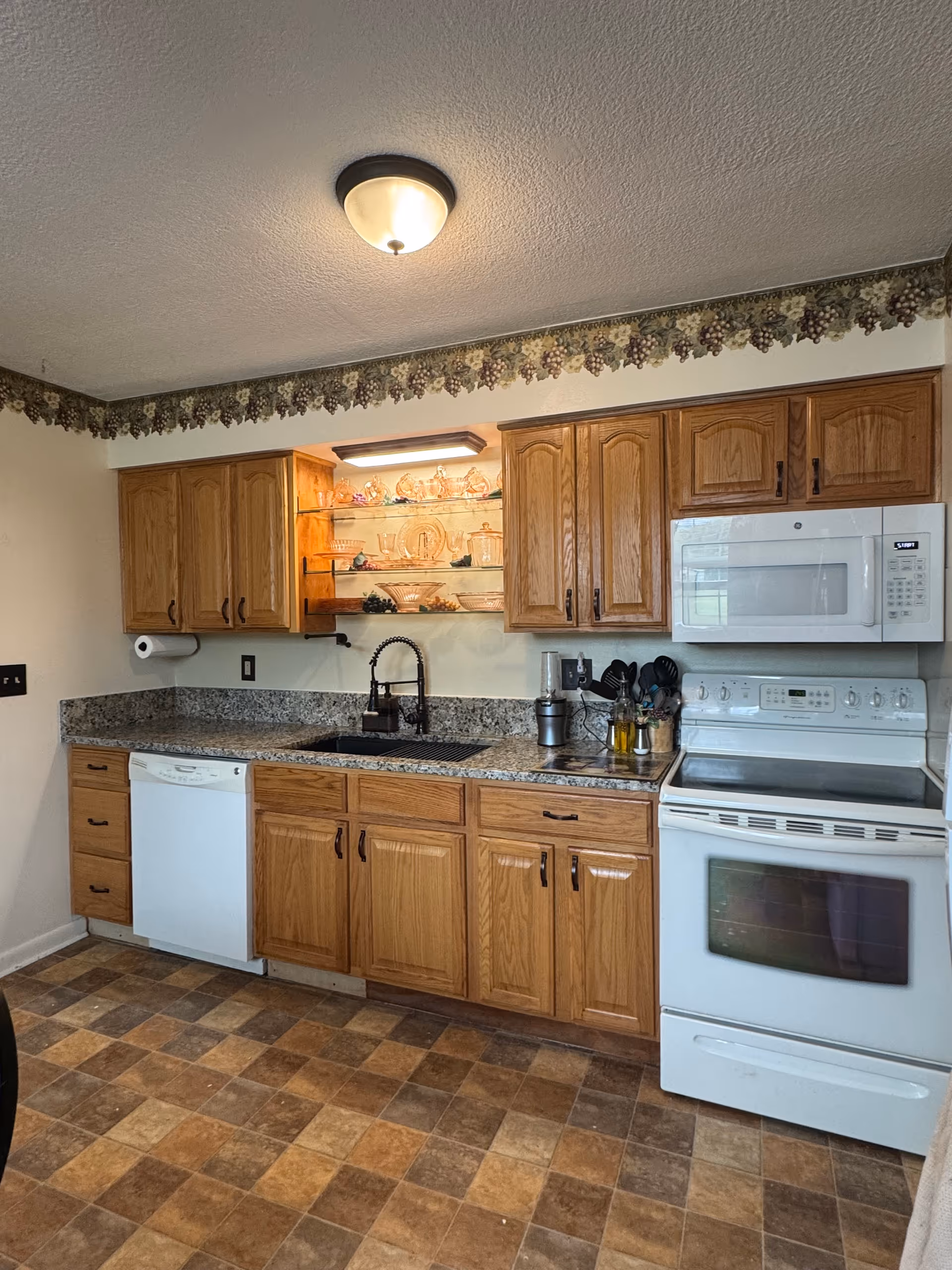 Kitchen area with wooden cabinets, granite counters, sink, dishwasher, microwave, and stove.