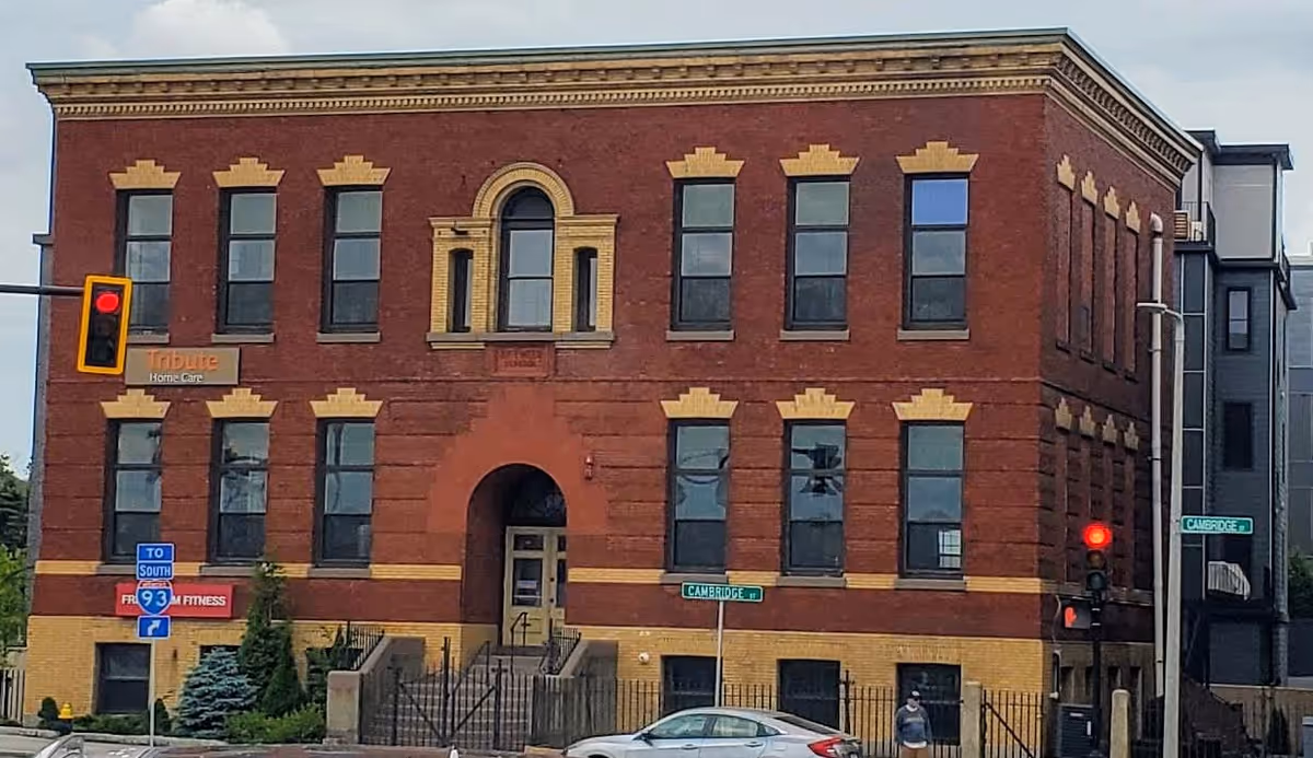 Brick three-story building labeled Tribute Home Care at a street corner.