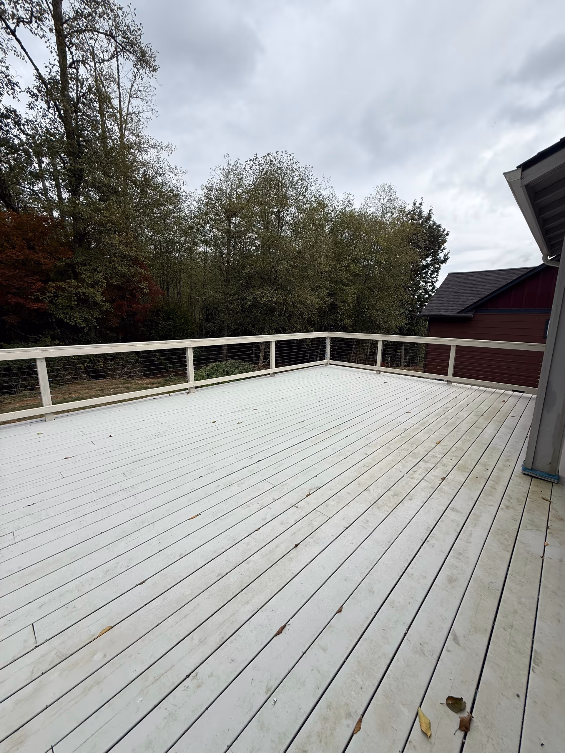 A large white wooden deck with railing overlooking trees under cloudy skies.