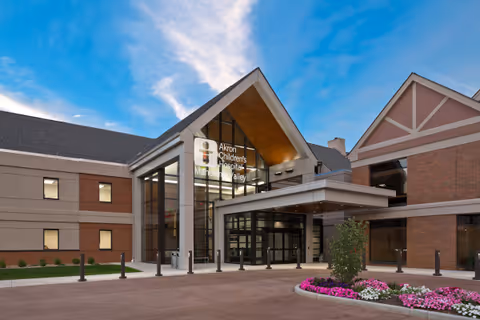 Modern hospital entrance with glass doors, peaked roof, and Akron Children's signage.