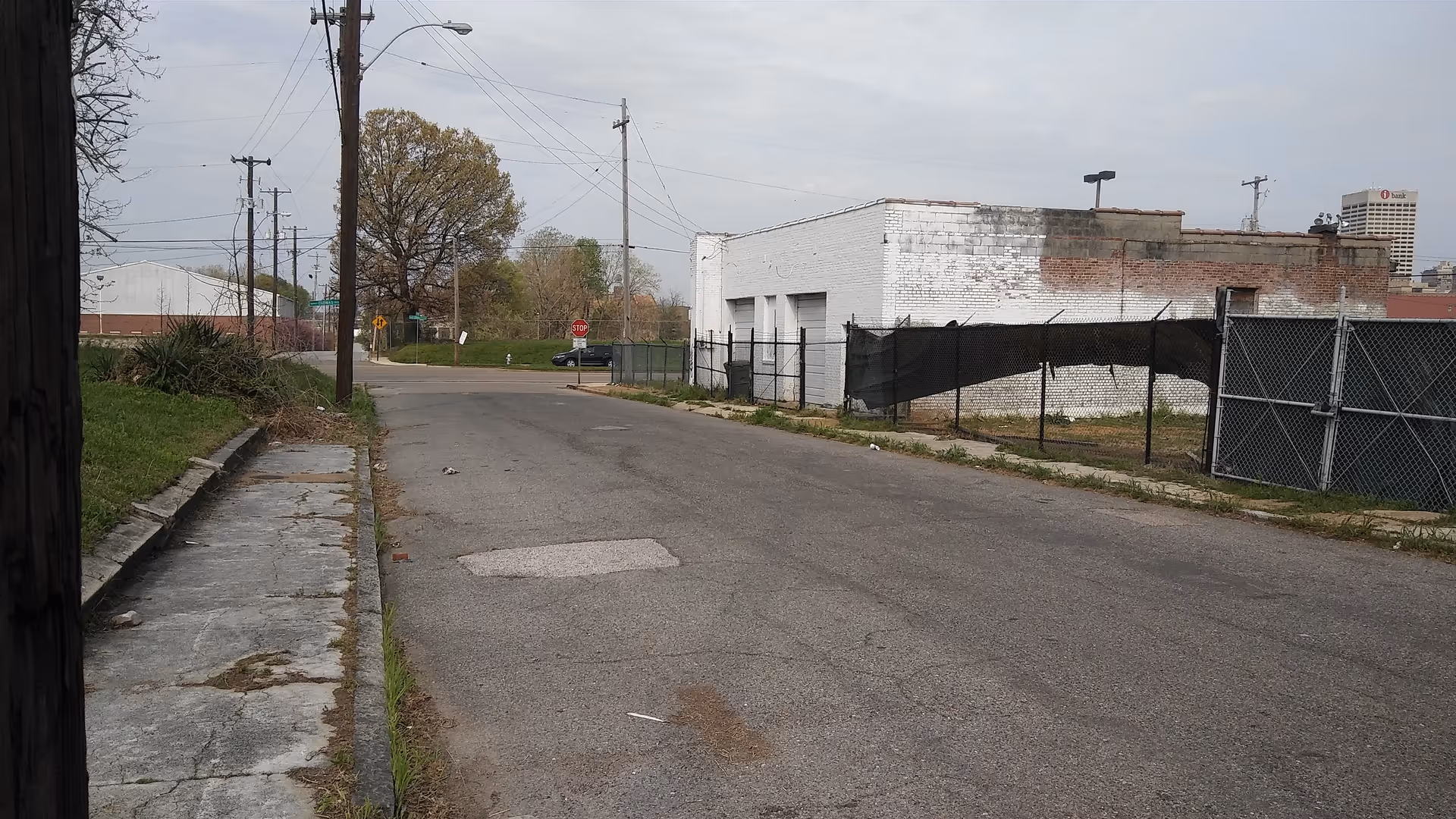 Deserted urban street with industrial buildings and a chain-link fence.