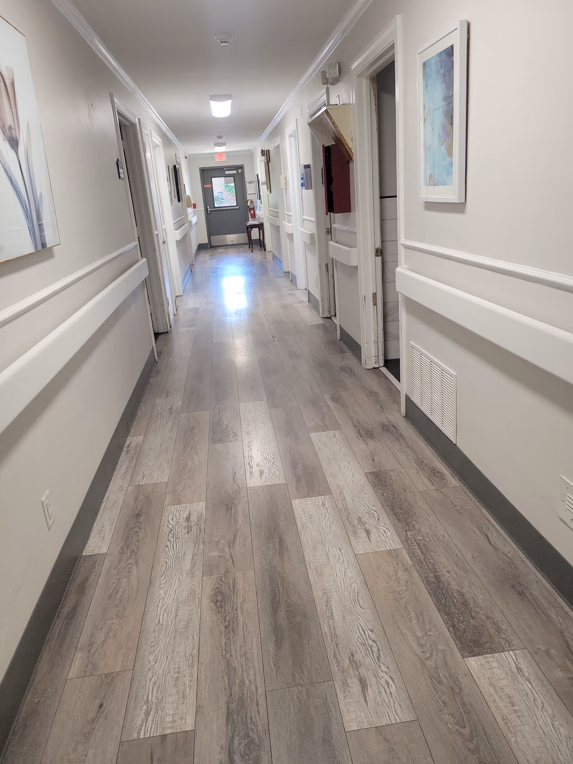 Long, well-lit corridor inside Alberta House with doors, wall art, and handrails.