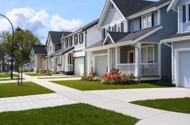 Row of modern gray townhomes with front porches, driveways, and manicured lawns.